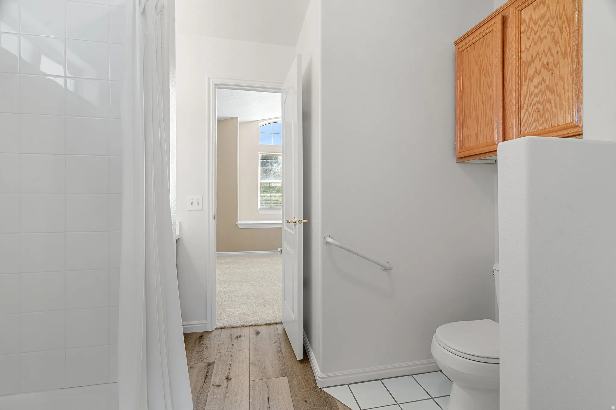 Bathroom featuring a shower/tub combination with white tile surround, wood-finish flooring, and a built-in wood cabinet