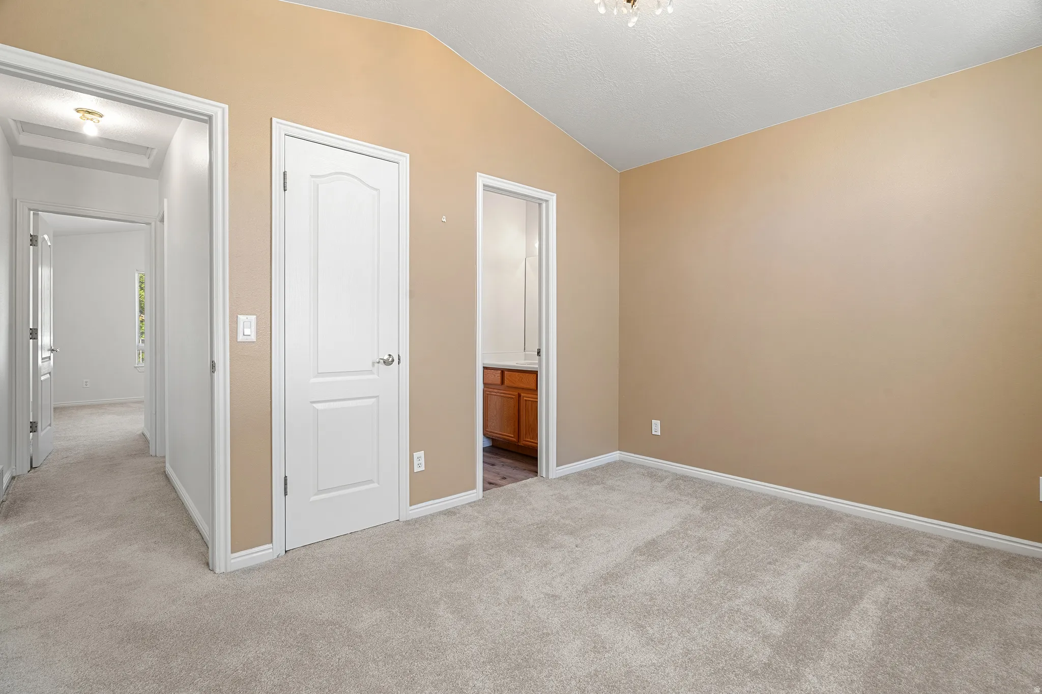 Spacious room featuring vaulted ceilings, light beige wall paint, and plush grey carpeting