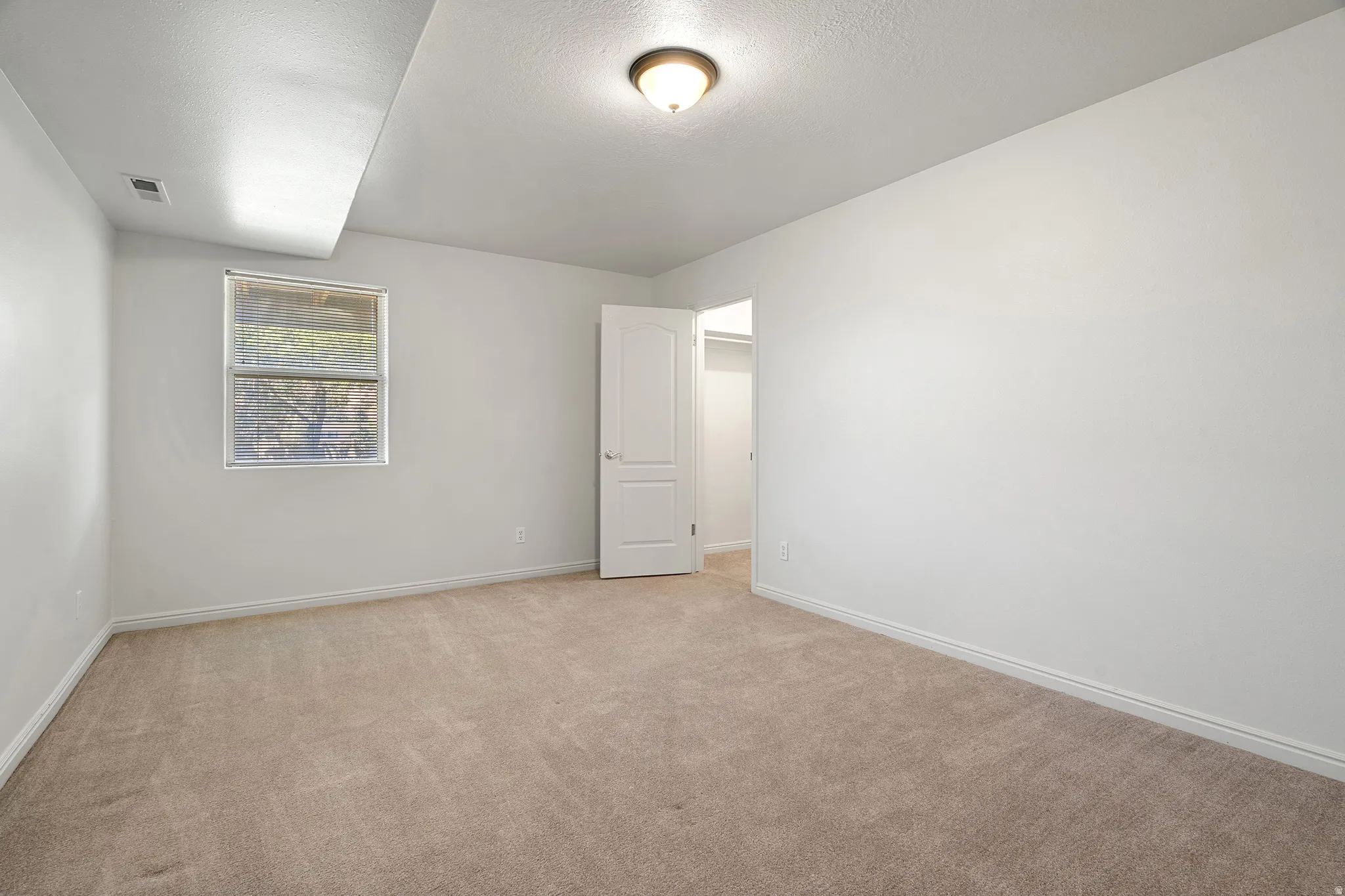 Spacious room featuring neutral carpeting, white wall finishes, and a single window offering exterior views