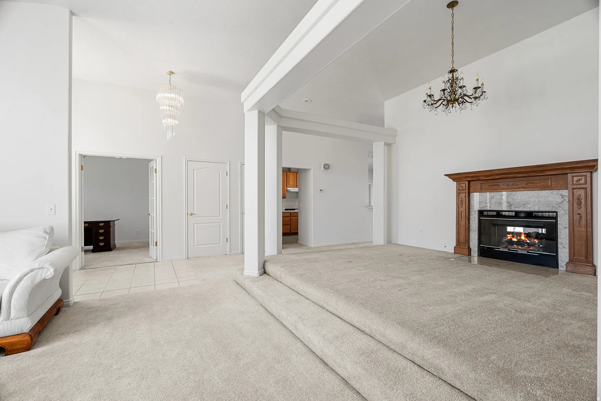 Two-tier living area featuring a fireplace with a wood-finish mantle, vaulted ceilings, and a tiered crystal chandelier