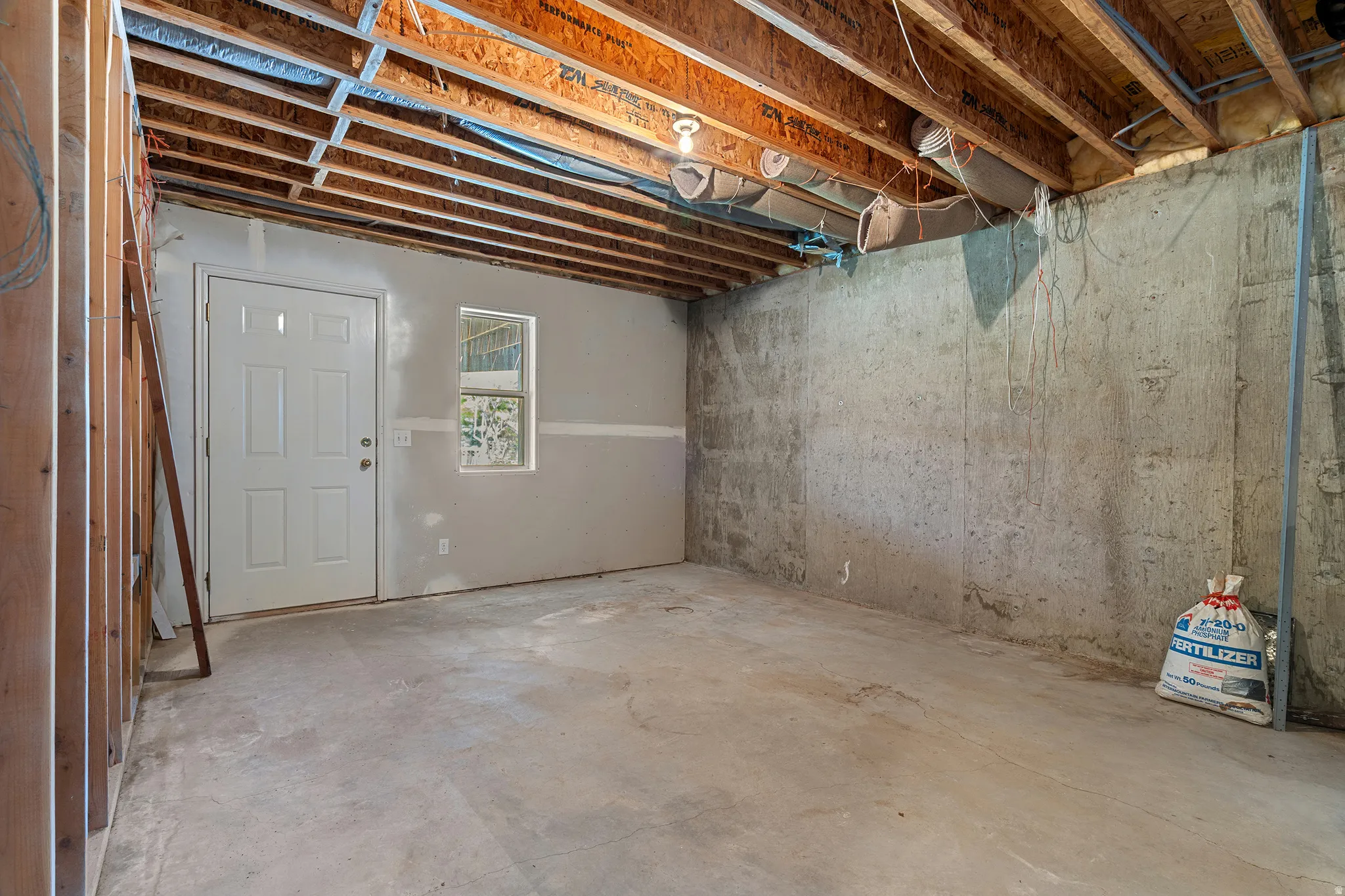 Unfinished basement space with exposed ceiling joists, concrete flooring, and a white paneled door