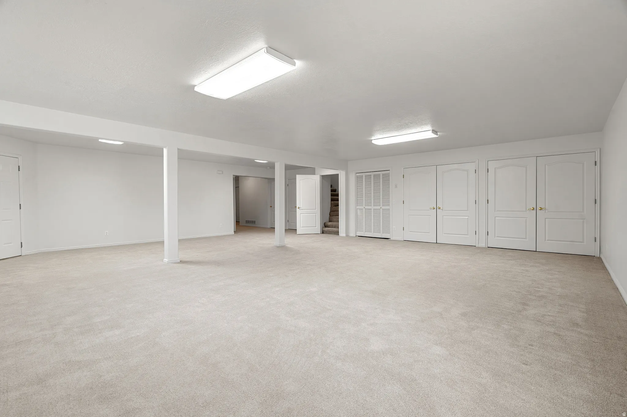 Expansive lower-level room featuring light neutral carpeting and white painted walls
