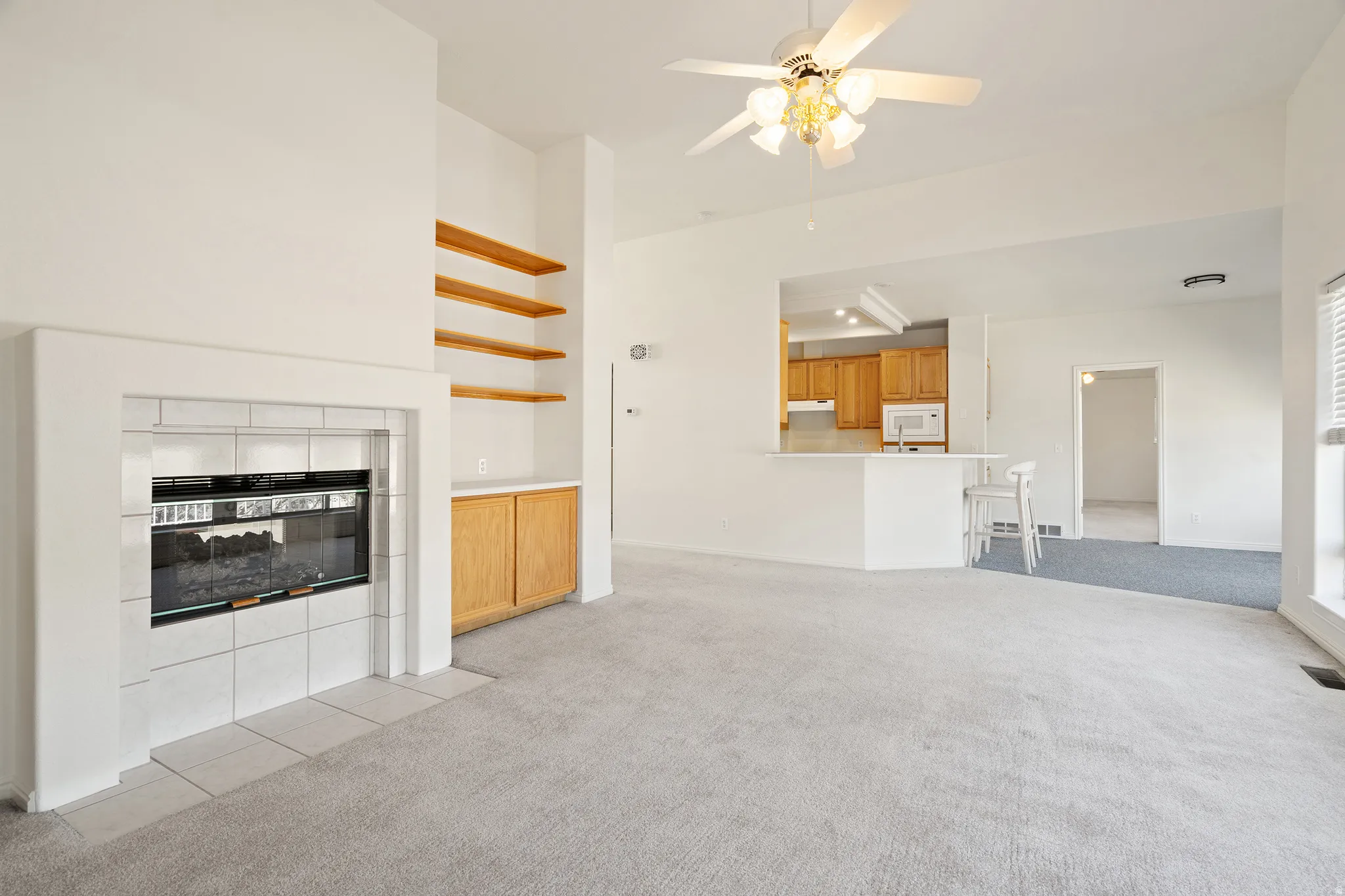 Bright living area featuring a tiled fireplace with an electric insert, built-in wooden shelving, and a ceiling fan with integrated lighting