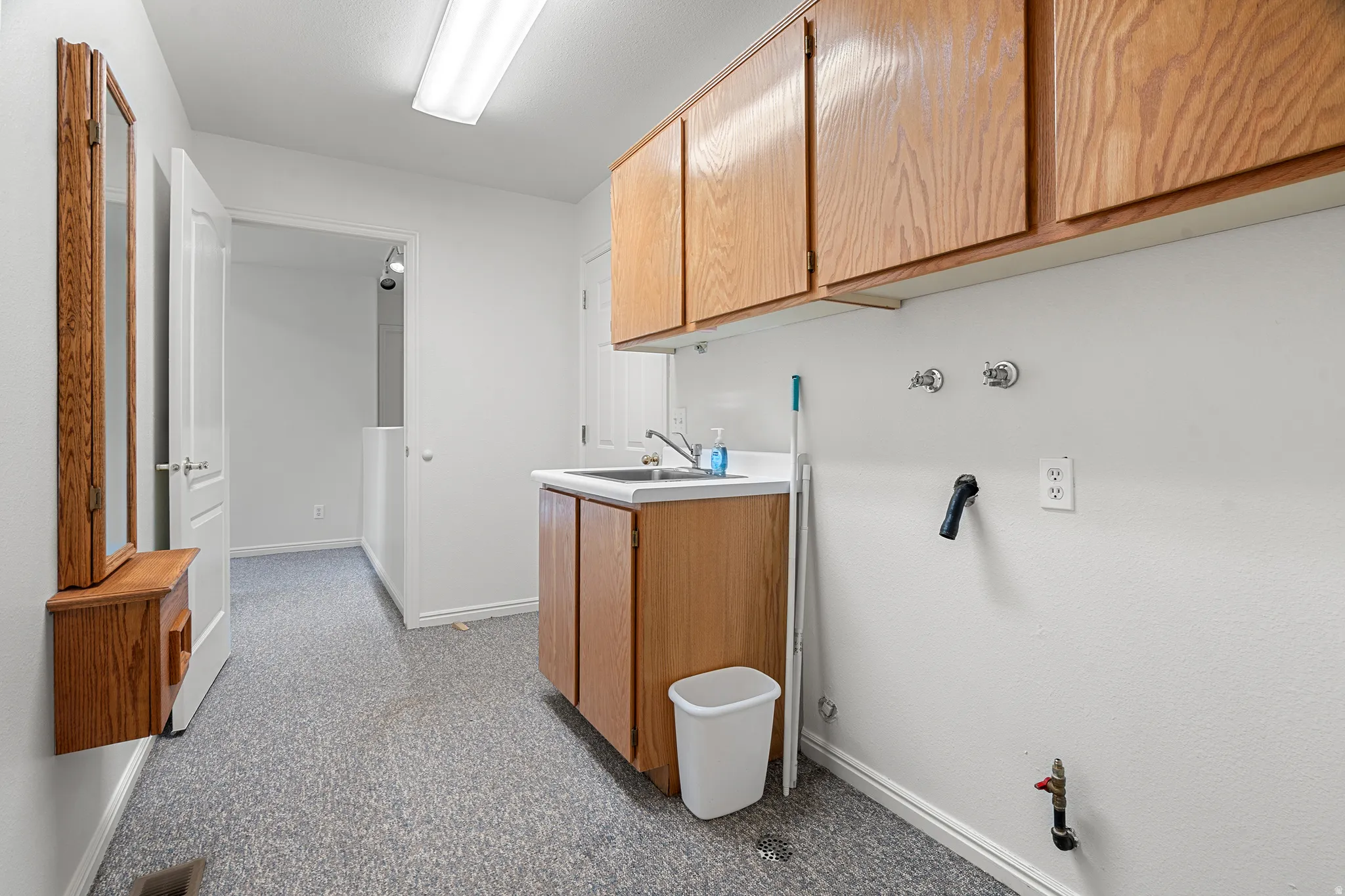 Laundry area featuring a utility sink, wood-finish cabinetry, and overhead fluorescent lighting