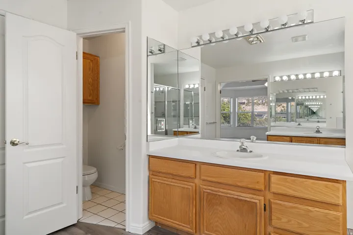 Bathroom vanity featuring a light-toned countertop with integrated sink, wood-finish cabinetry, and an expansive wall-mounted mirror