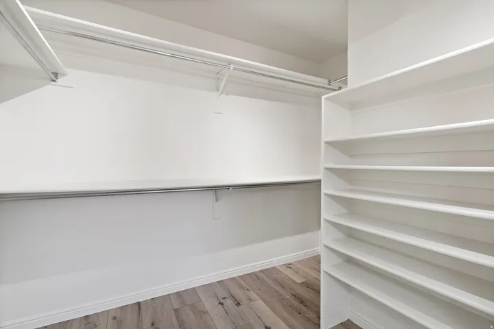 Walk-in closet featuring light wood-finish flooring, white baseboards, multiple white shelving units, and chrome hanging rods