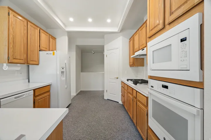Kitchen featuring light wood cabinetry, white countertops, built-in white appliances, including an oven and microwave, and recessed lighting