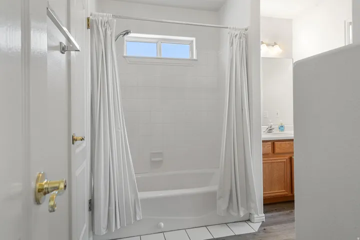 Bathtub and shower combination with white tile surround, transom window, and white shower curtain