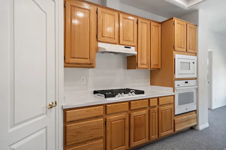 Kitchen featuring wood-finish cabinetry, white countertops, a built-in wall oven, a built-in microwave, and a gas cooktop with an overhead range hood