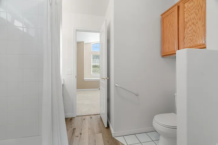 Bathroom featuring a shower/tub combination with white tile surround, wood-finish flooring, and a built-in wood cabinet