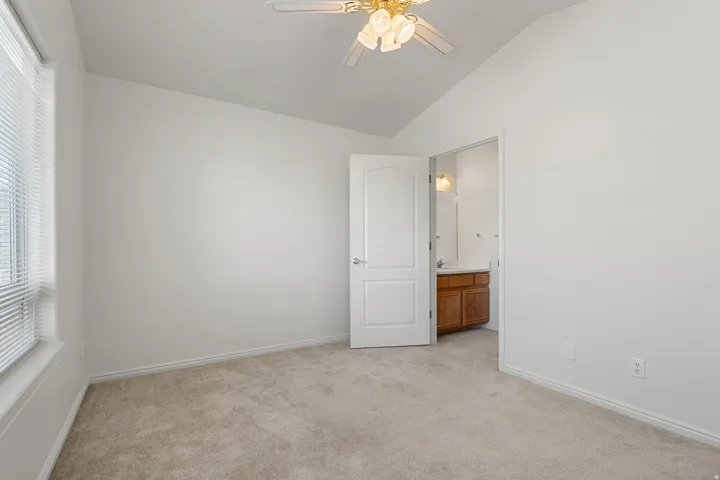 Carpeted room featuring a vaulted ceiling and a ceiling fan with integrated lighting