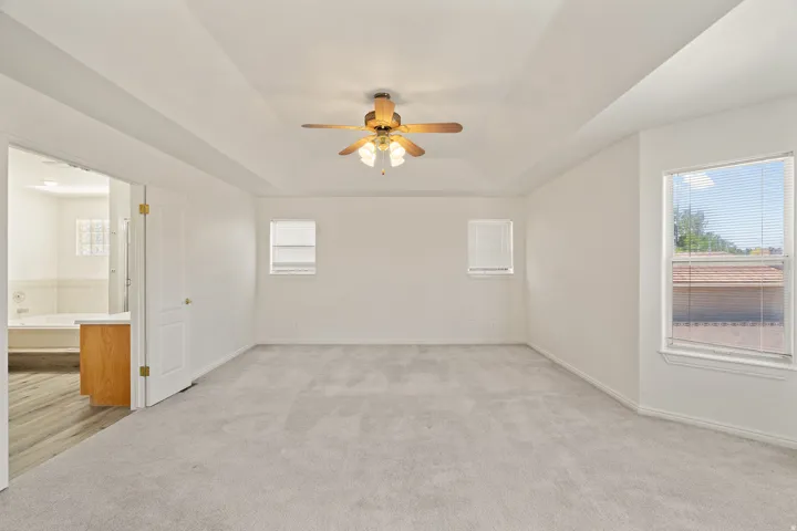 Spacious room featuring light gray carpet flooring, tray ceiling, and a ceiling fan with integrated lighting