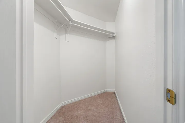 Walk-in closet featuring light brown carpeting, white baseboards, and built-in white shelving