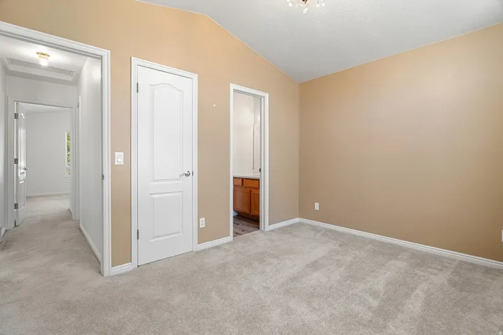 Spacious room featuring vaulted ceilings, light beige wall paint, and plush grey carpeting