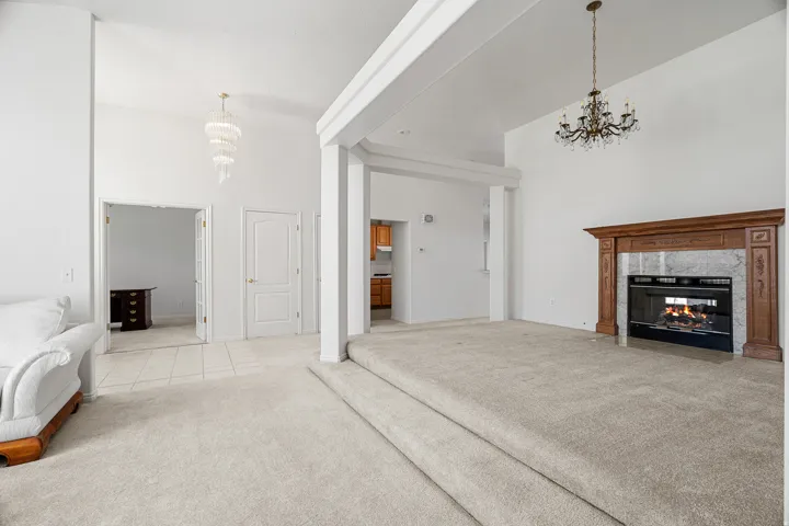 Two-tier living area featuring a fireplace with a wood-finish mantle, vaulted ceilings, and a tiered crystal chandelier