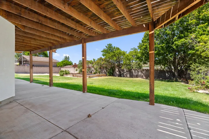 Expansive concrete patio with a wooden pergola, overlooking a spacious lawn