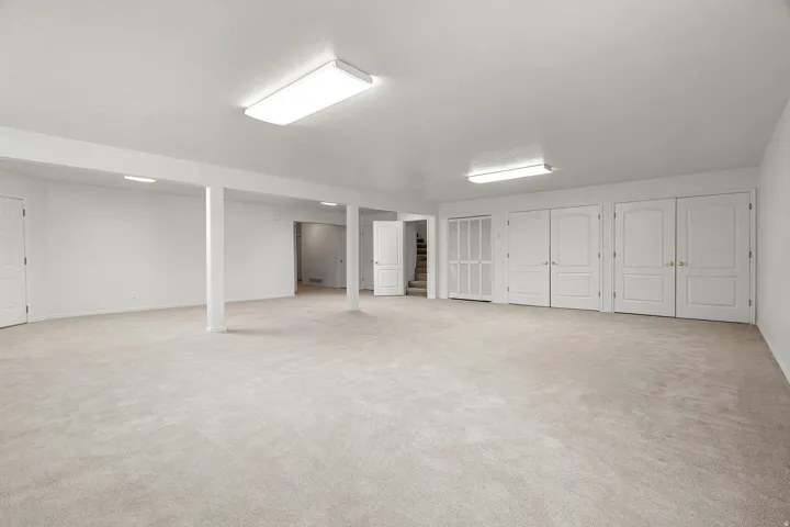 Expansive lower-level room featuring light neutral carpeting and white painted walls