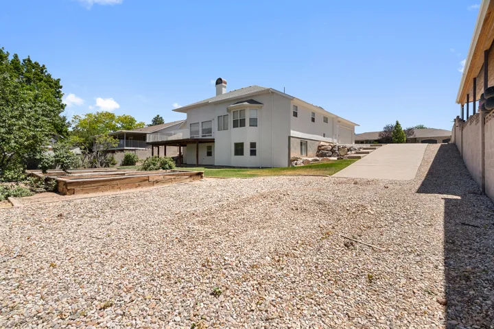 Expansive gravel yard featuring a concrete driveway, raised garden beds, and a white stucco exterior with a multi-level deck