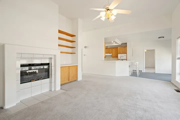 Bright living area featuring a tiled fireplace with an electric insert, built-in wooden shelving, and a ceiling fan with integrated lighting