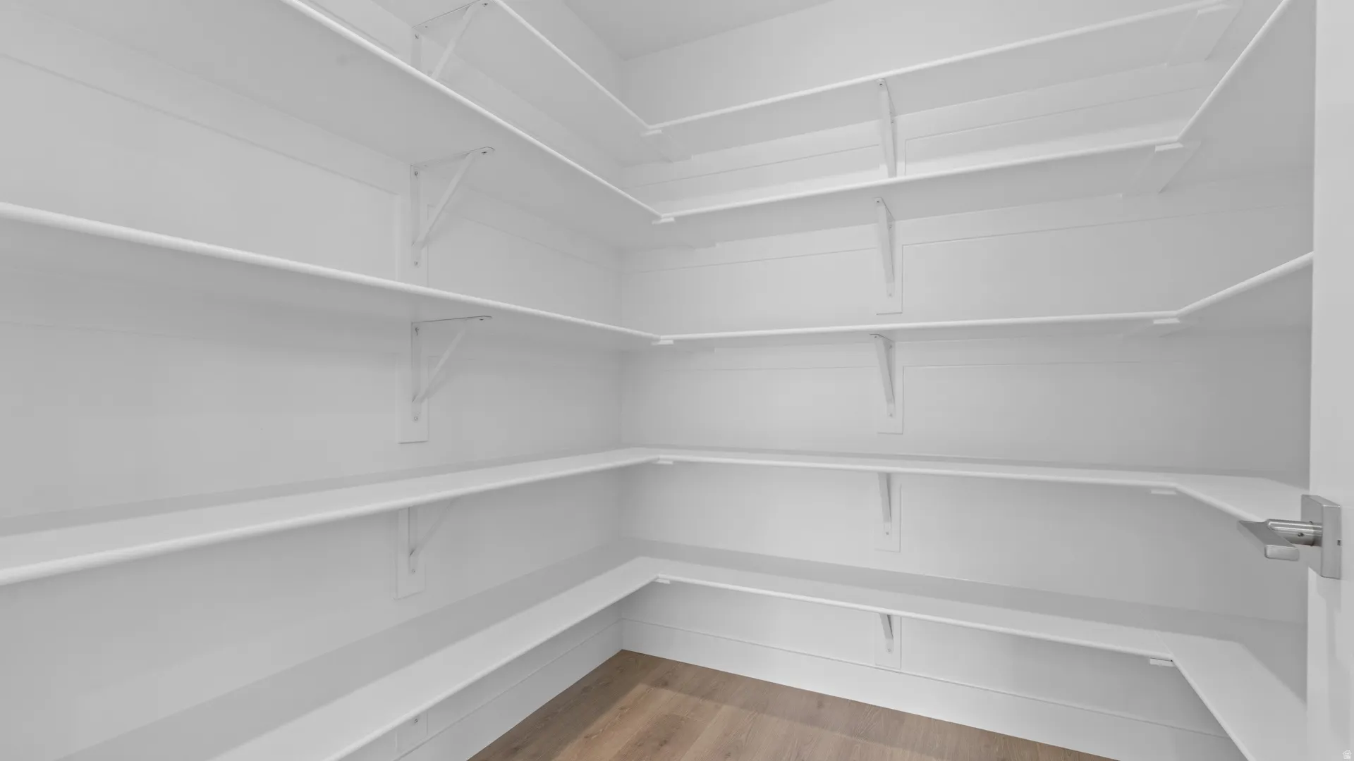 Expansive corner pantry featuring white shelving, multiple storage tiers, and wood-finish flooring
