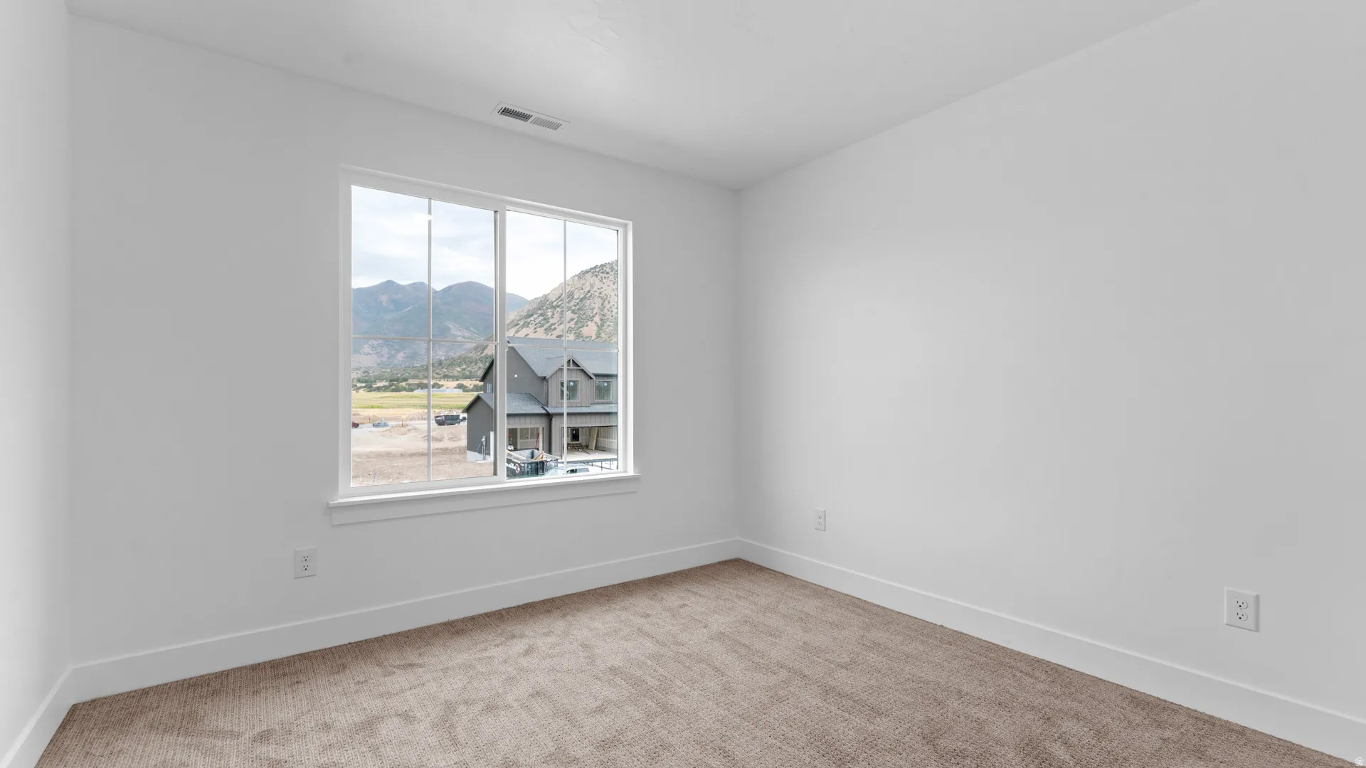 Bright interior space featuring a large window, neutral wall paint, white trim, and a textured carpet