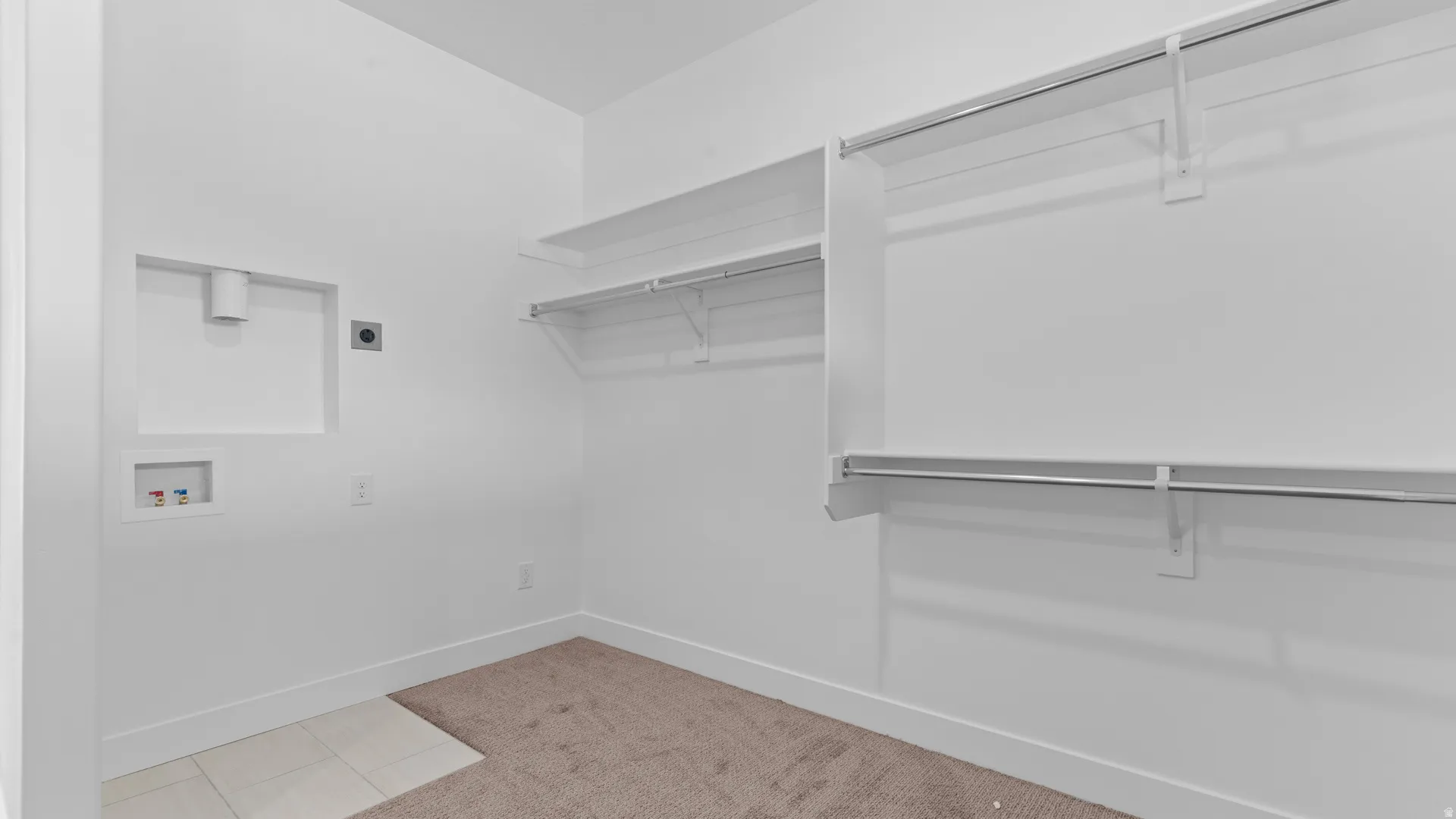 Dedicated laundry area featuring a tile floor section, wall connections for washer and dryer, and integrated shelving with hanging rods