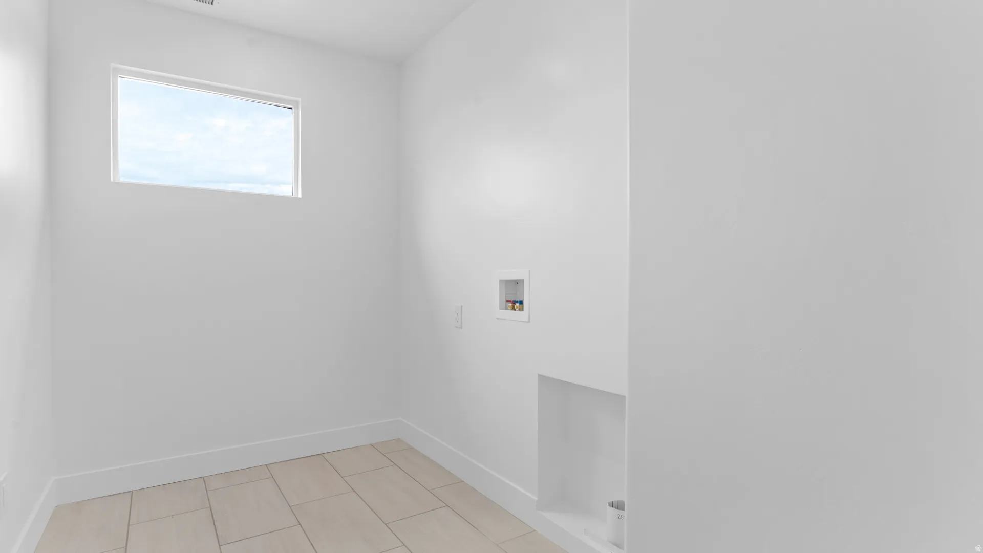 Utility room featuring light-toned tile flooring, a horizontal window, and white baseboards