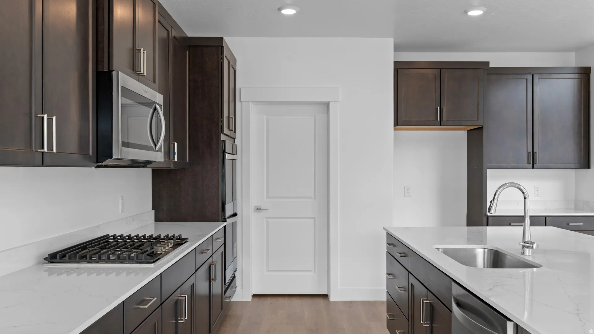Contemporary kitchen featuring dark wood cabinetry, white countertops, stainless steel appliances, a gas cooktop, and a kitchen island with an undermount sink