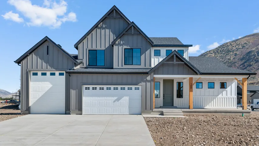 Contemporary farmhouse exterior featuring board-and-batten siding, a dark asphalt shingle roof, a covered front porch with natural wood posts, a two-car garage, and a concrete driveway