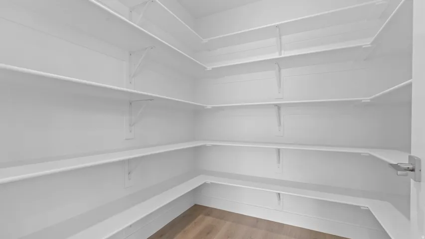 Expansive corner pantry featuring white shelving, multiple storage tiers, and wood-finish flooring