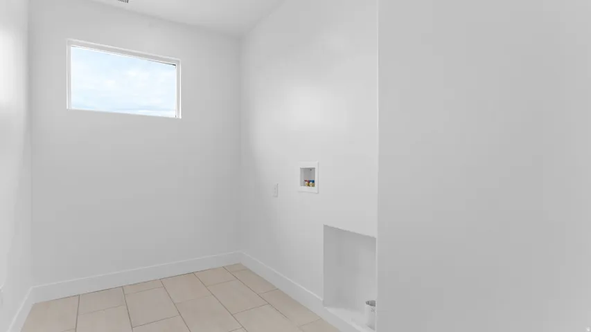 Utility room featuring light-toned tile flooring, a horizontal window, and white baseboards