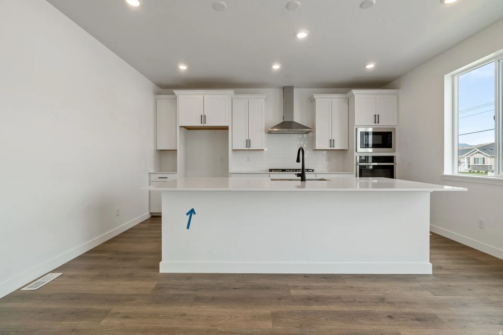 Modern kitchen featuring a large central island with a solid surface countertop, white shaker cabinetry, stainless steel appliances, and wood-finish flooring