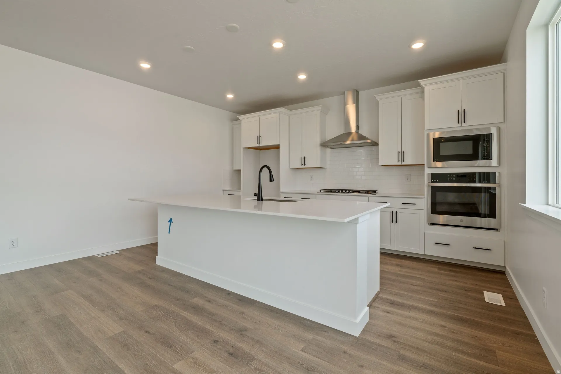 Kitchen featuring a large central island with a sink, white cabinetry, stainless steel appliances, wood-finish flooring, and recessed lighting