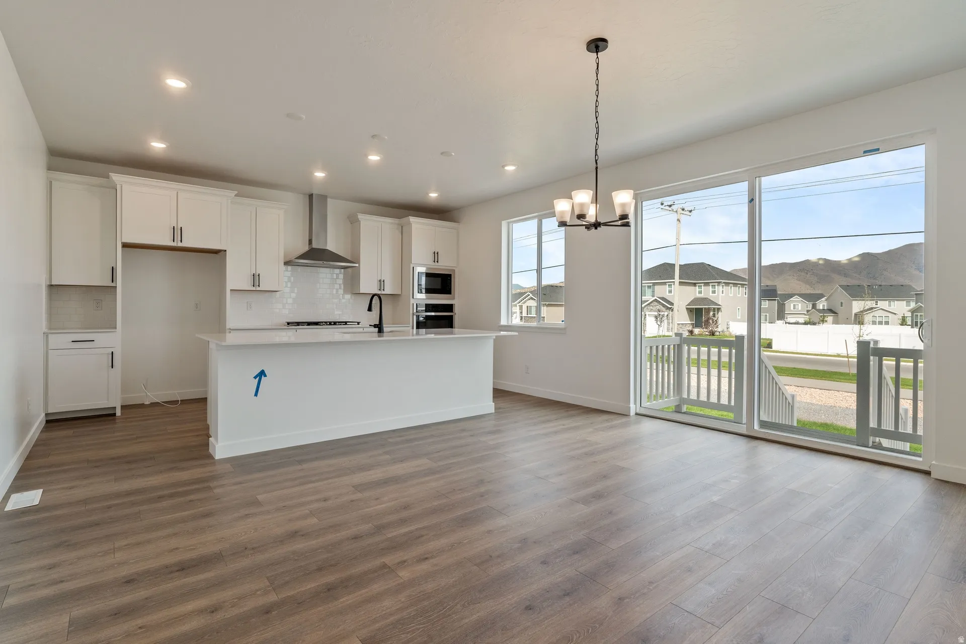 Open-concept living space with wood-finish flooring, a contemporary kitchen island, white cabinetry, integrated double ovens, and large sliding glass doors leading to an outdoor deck