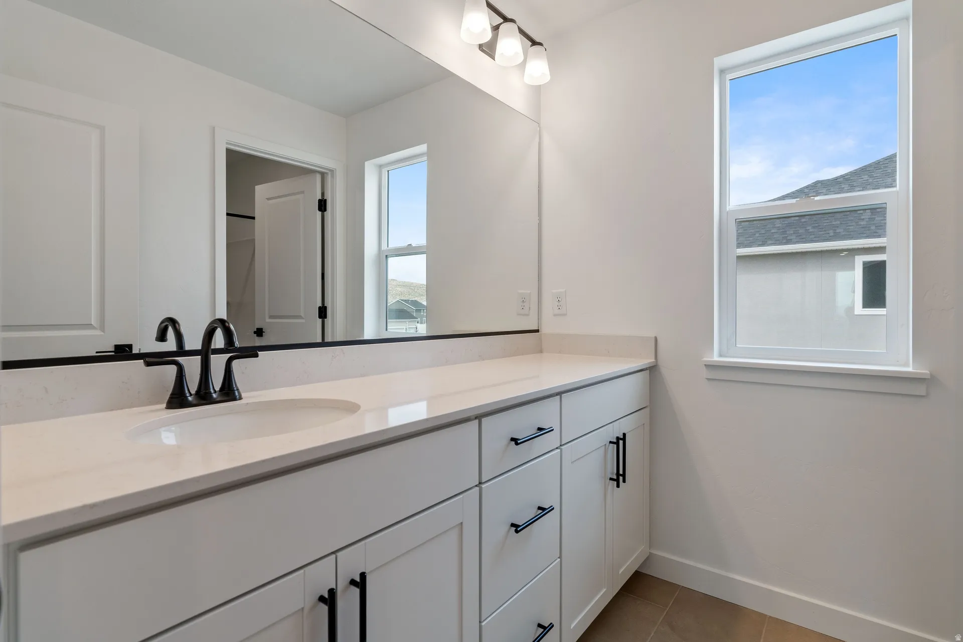 Bathroom vanity featuring a light-toned countertop, dual rectangular sinks with matte black fixtures, white cabinetry, and a large mirror