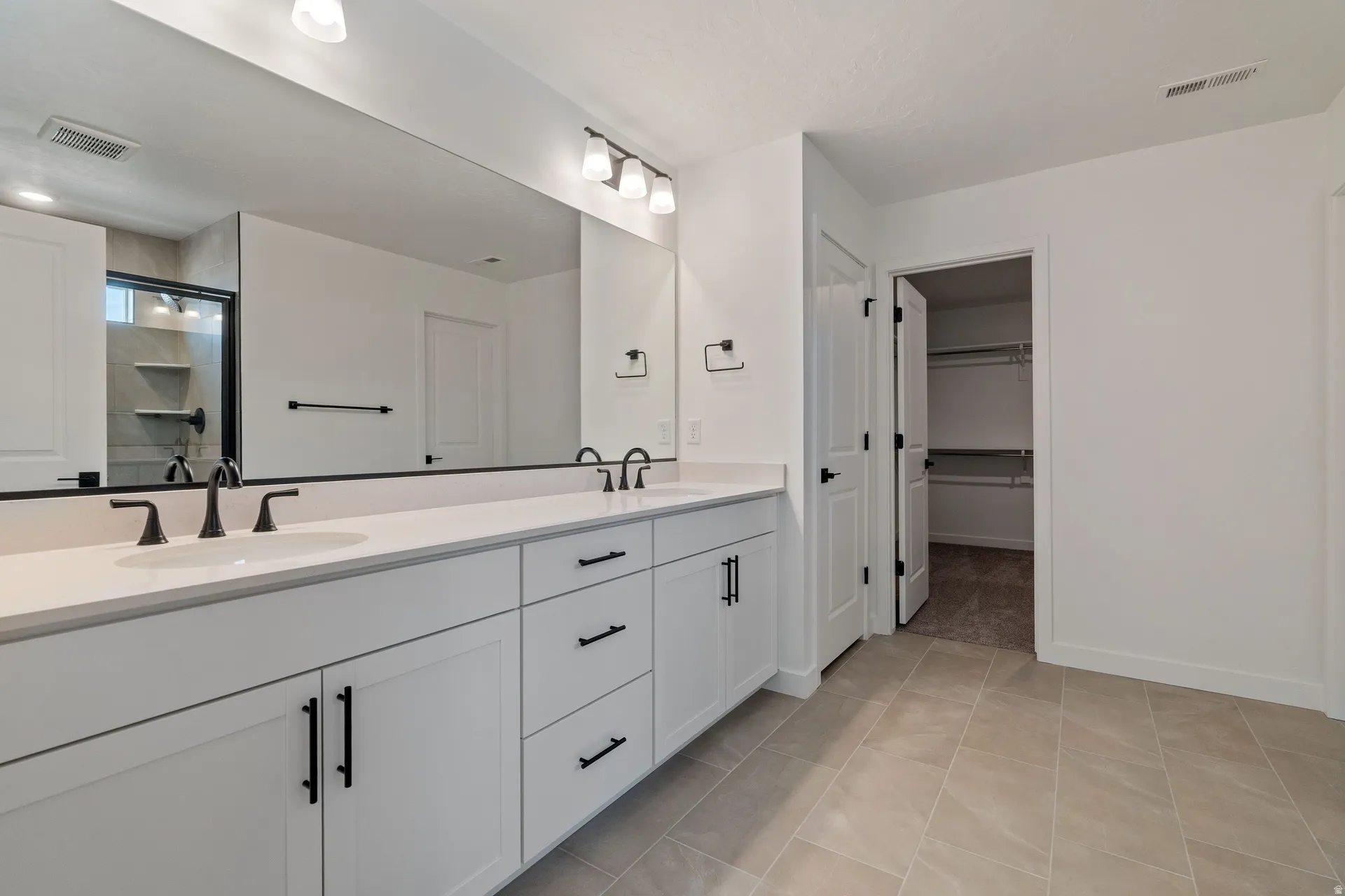 Dual vanity with white cabinetry, matte black hardware, and an expansive mirror