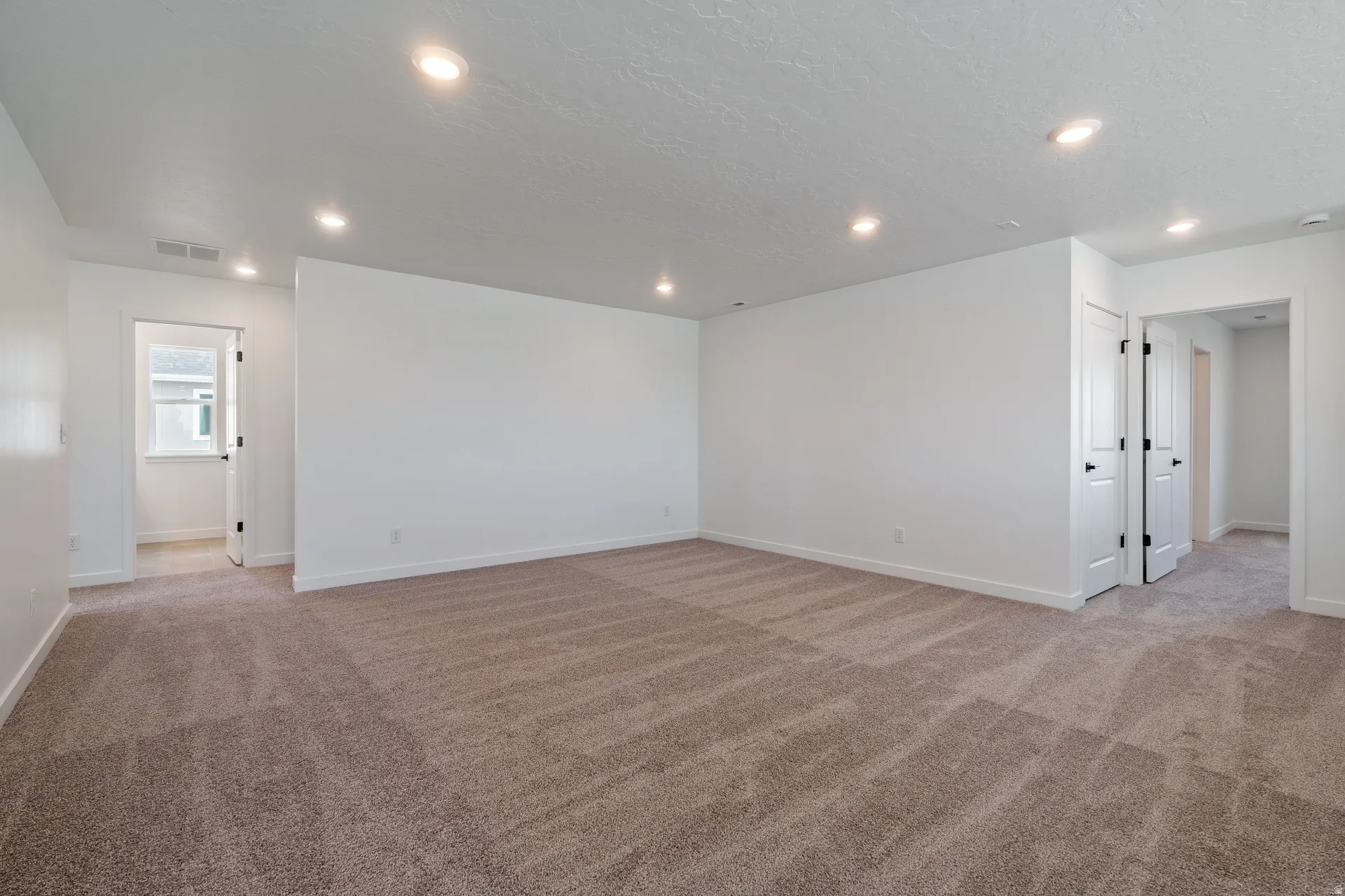 Spacious room featuring plush carpeting, crisp white walls, recessed lighting, and multiple entryways with white doors and matte black hardware