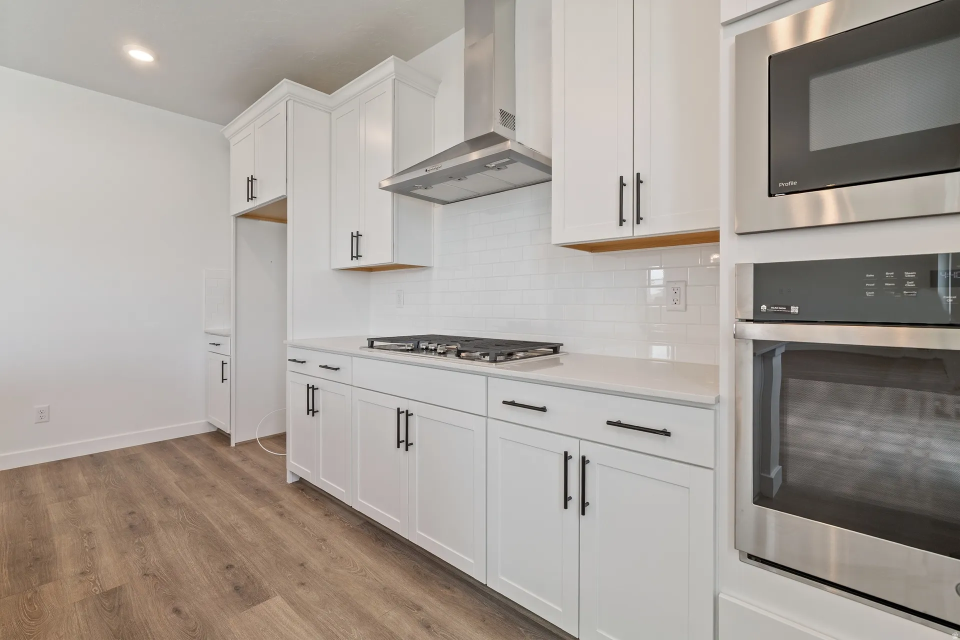 Modern kitchen featuring white shaker cabinetry, stainless steel appliances, a subway tile backsplash, and wood-finish flooring