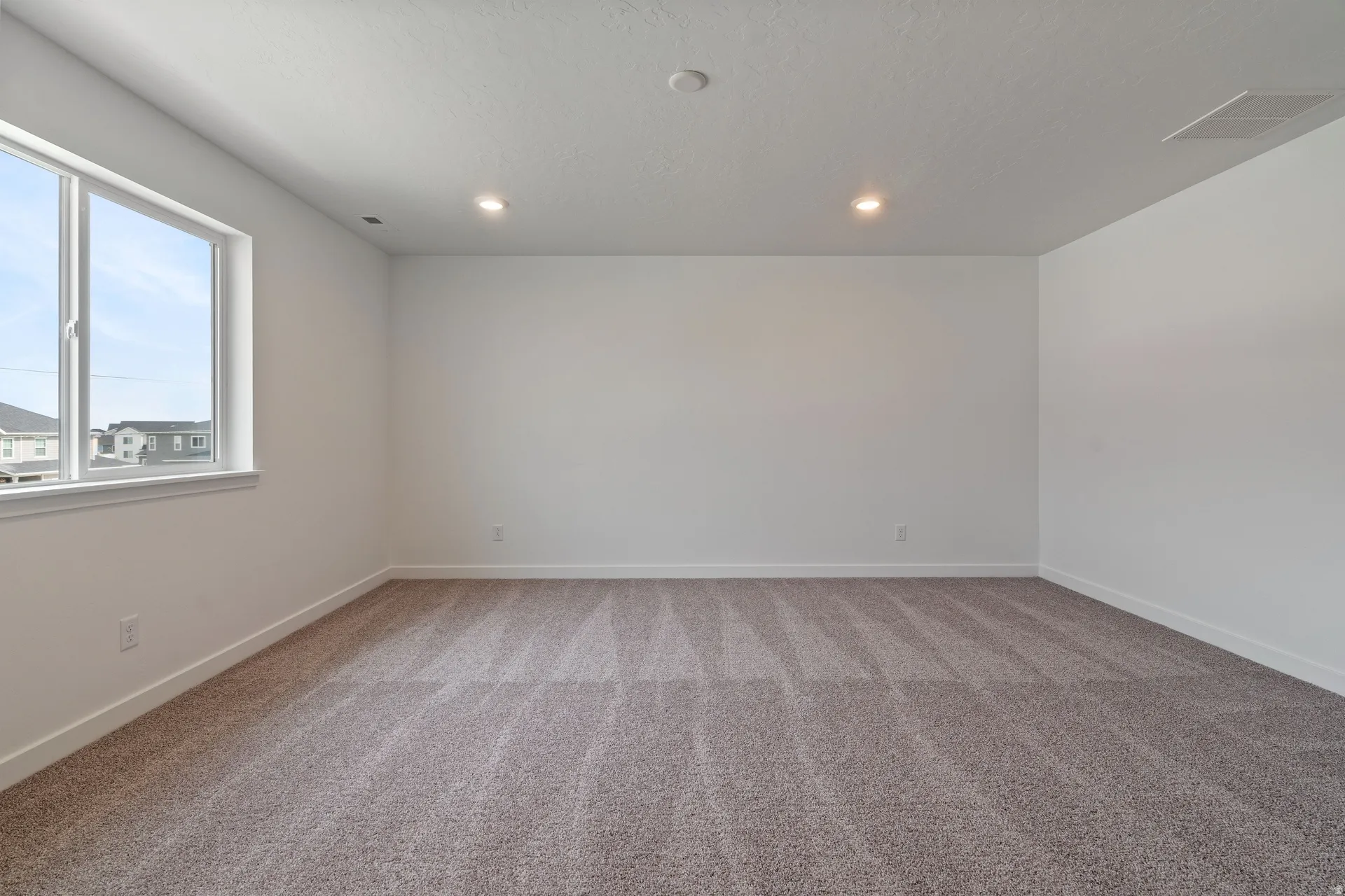 Spacious room featuring neutral carpeting, white walls, recessed lighting, and a large window providing ample natural light