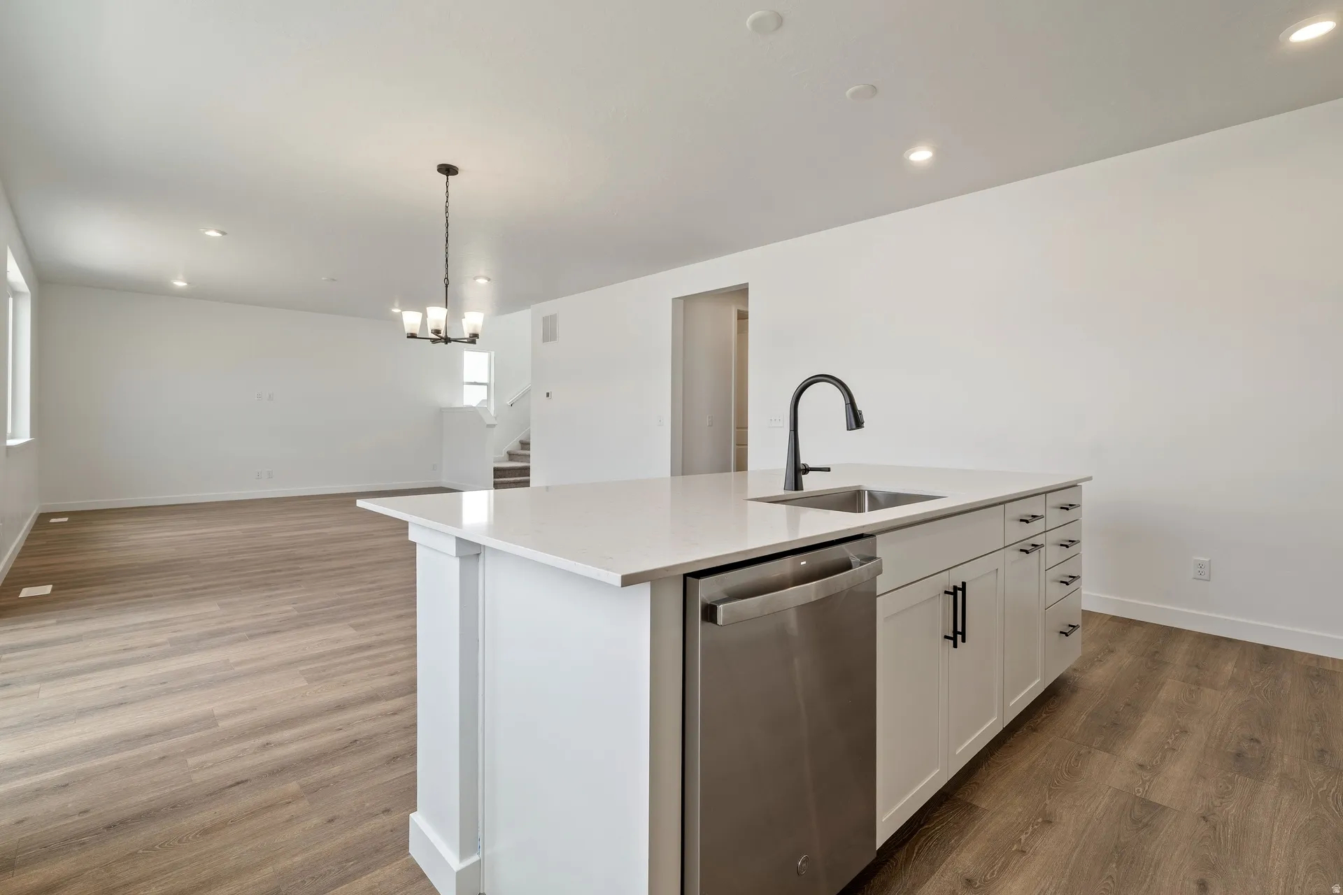 Central kitchen island featuring a stainless steel sink with a matte black faucet, integrated dishwasher, and white cabinetry