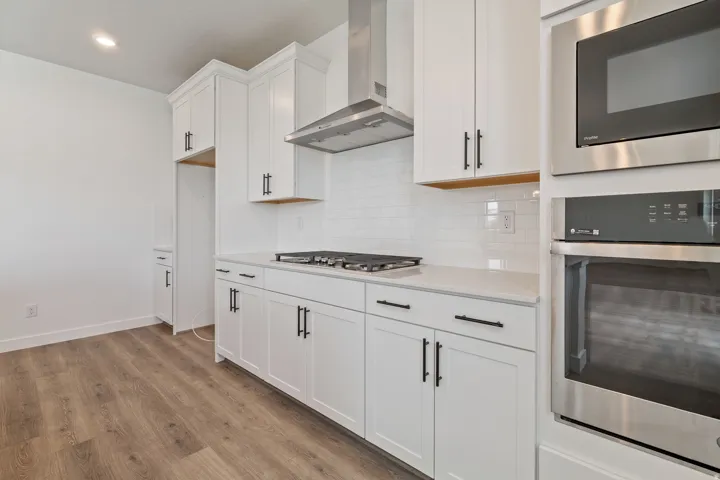 Modern kitchen featuring white shaker cabinetry, stainless steel appliances, a subway tile backsplash, and wood-finish flooring
