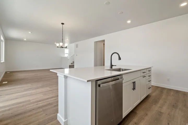 Central kitchen island featuring a stainless steel sink with a matte black faucet, integrated dishwasher, and white cabinetry