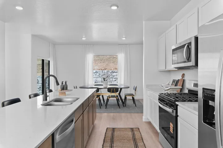 Bright kitchen featuring an expansive island with an undermount sink and matte black faucet, quartz countertops, a full suite of stainless steel appliances, and abundant white cabinetry