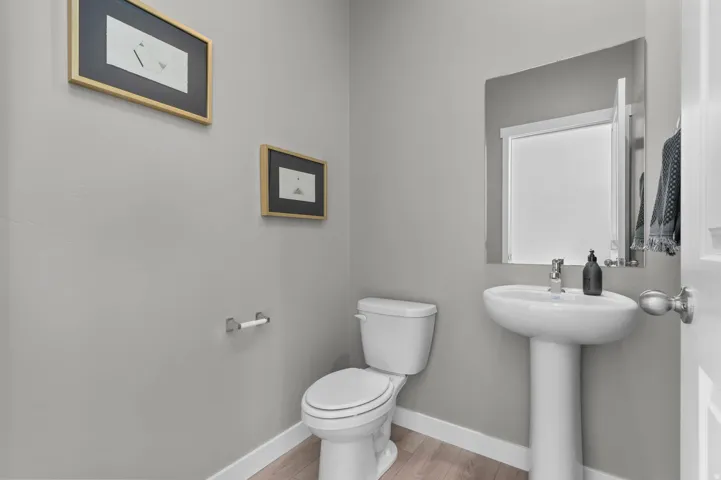 Pedestal sink with chrome faucet and mirror, complemented by light wood-finish flooring and a white toilet