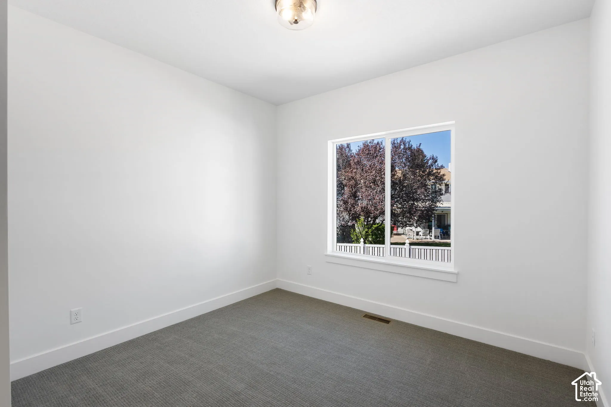 Neutral white walls and ceiling, gray carpet flooring, contemporary light fixture, and a large window with white trim