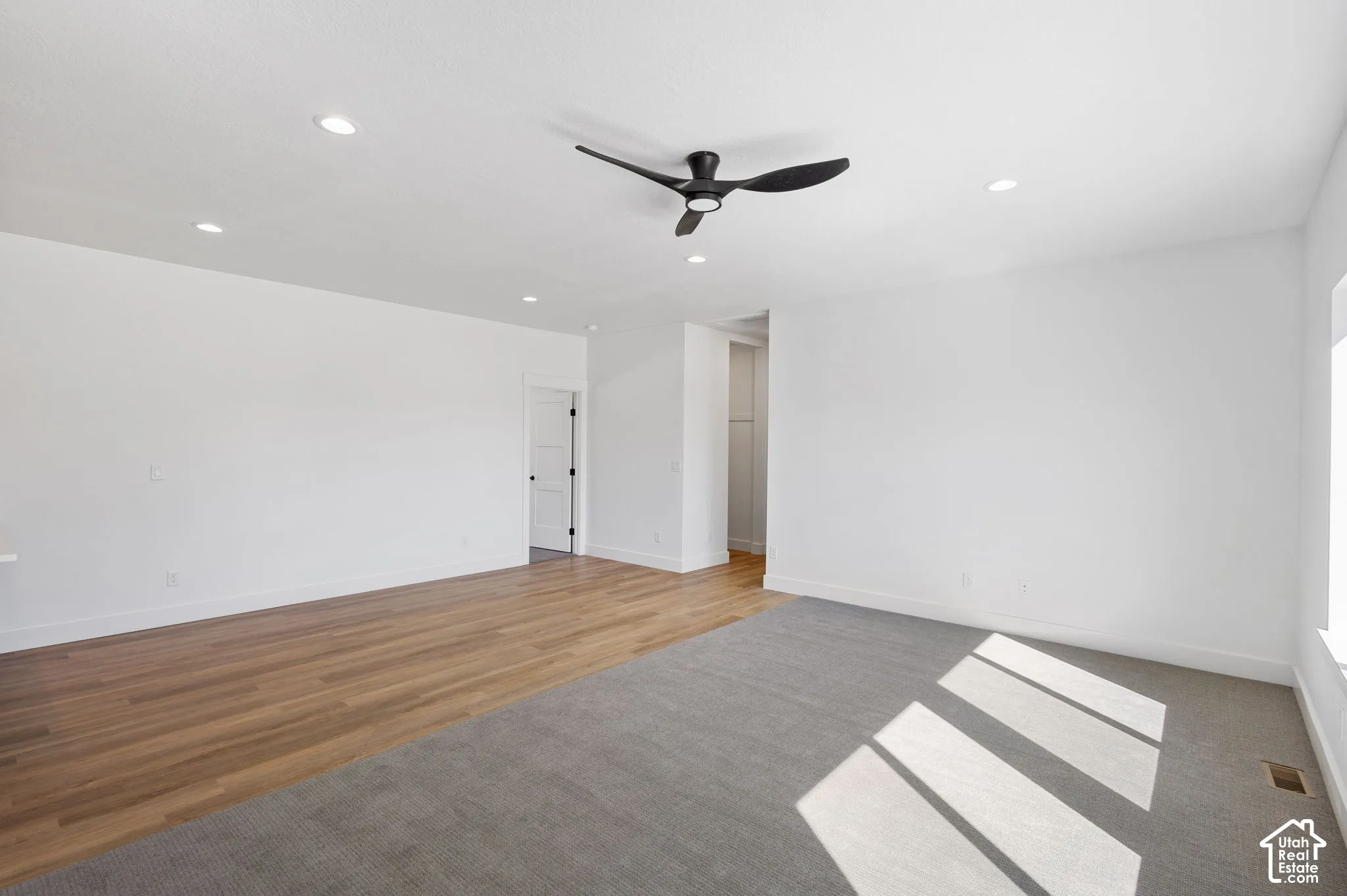 Recessed lighting, wood-finish flooring, gray carpeting, a ceiling fan, and a white interior door with dark hardware