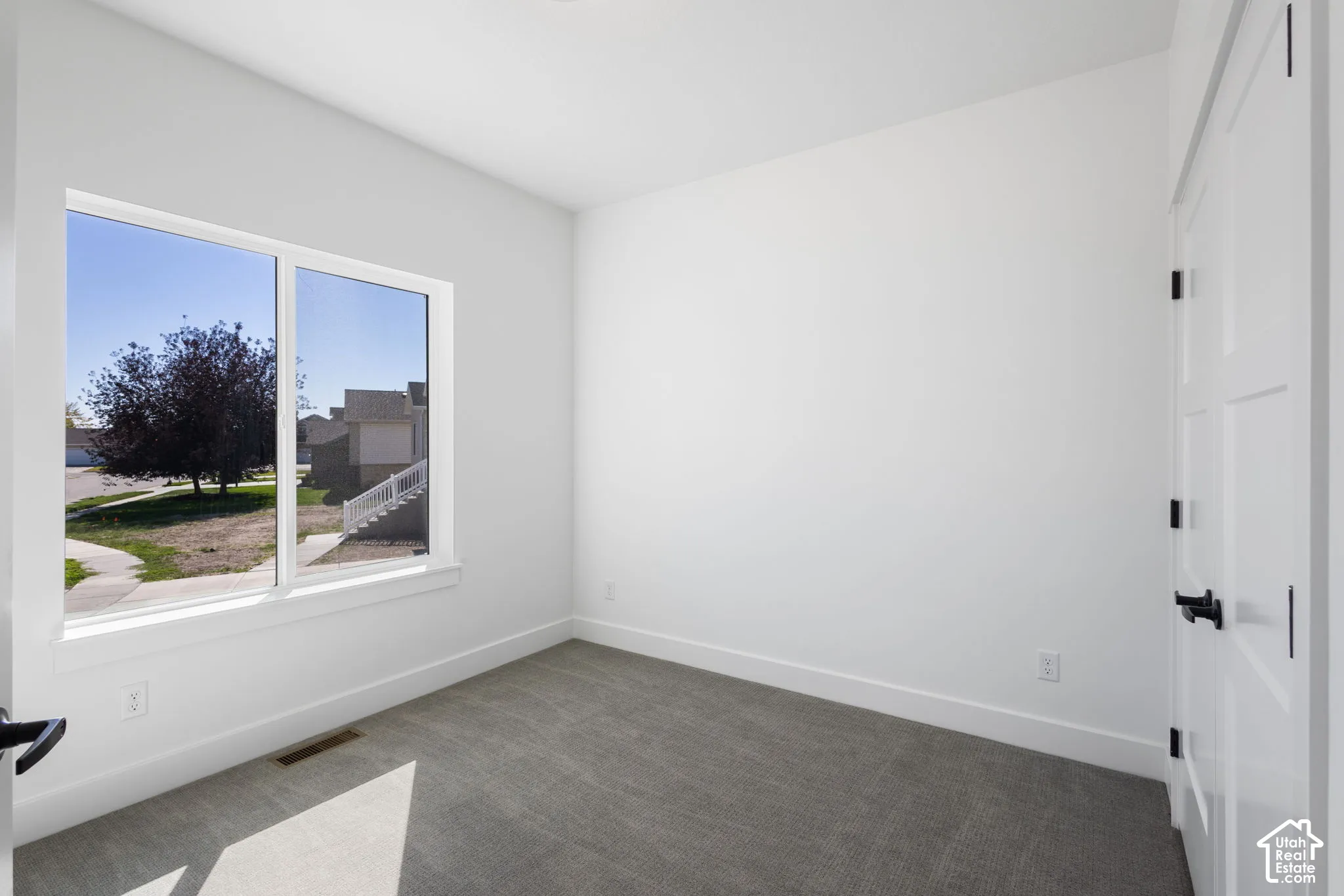 White walls featuring a large window, gray carpet, and white paneled doors with black hardware