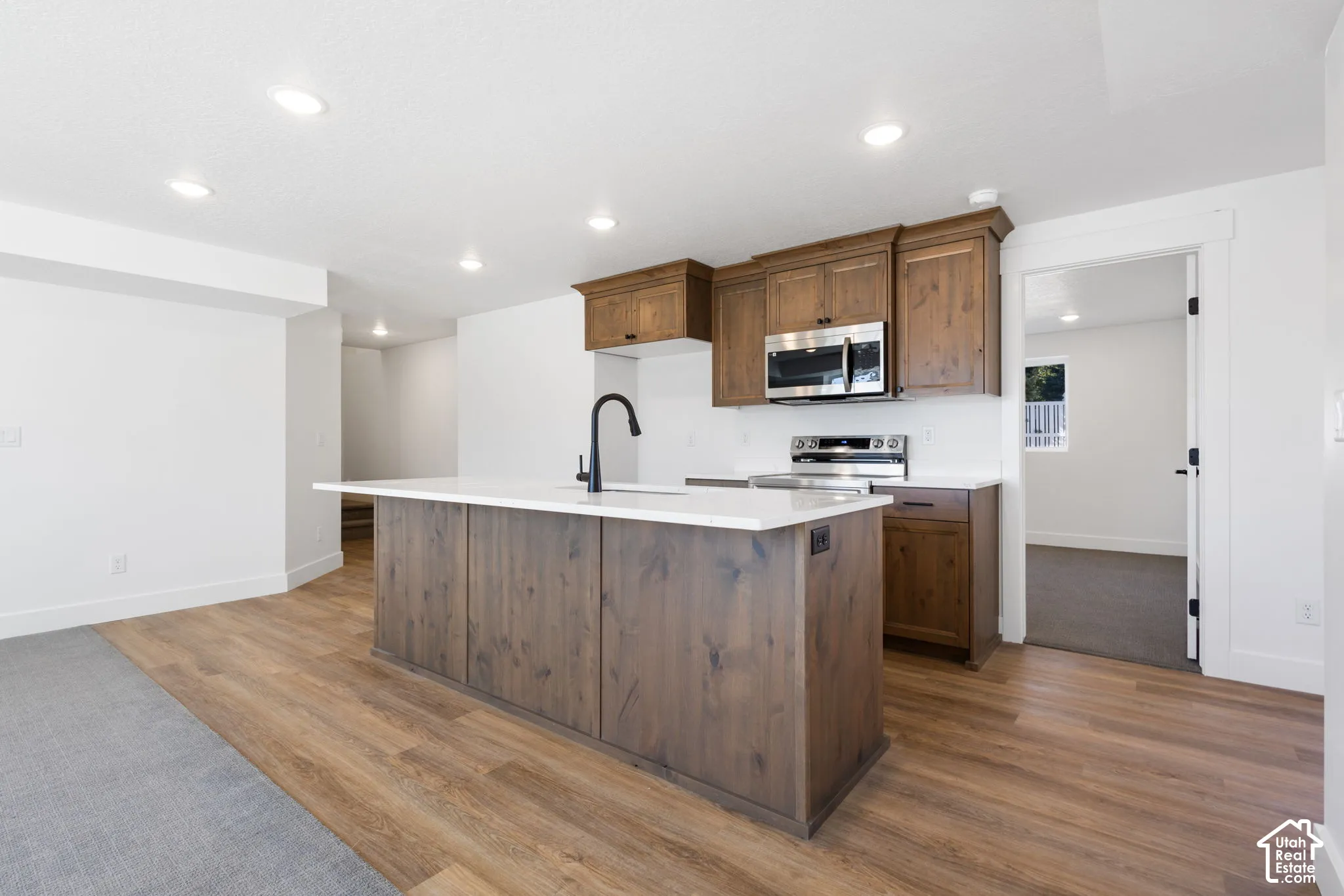 Kitchen featuring a central island with a sink, wood-finish cabinetry, stainless steel appliances, and recessed lighting