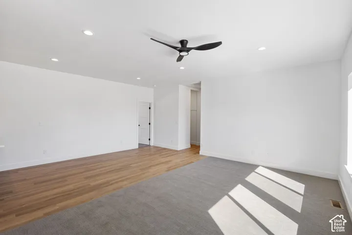 Recessed lighting, wood-finish flooring, gray carpeting, a ceiling fan, and a white interior door with dark hardware