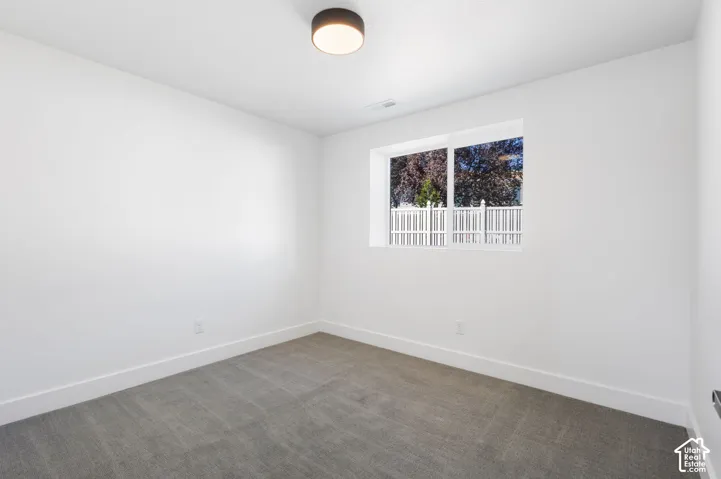 Neutral color palette, window with exterior fencing, flush-mount ceiling light, white trim, and gray carpet